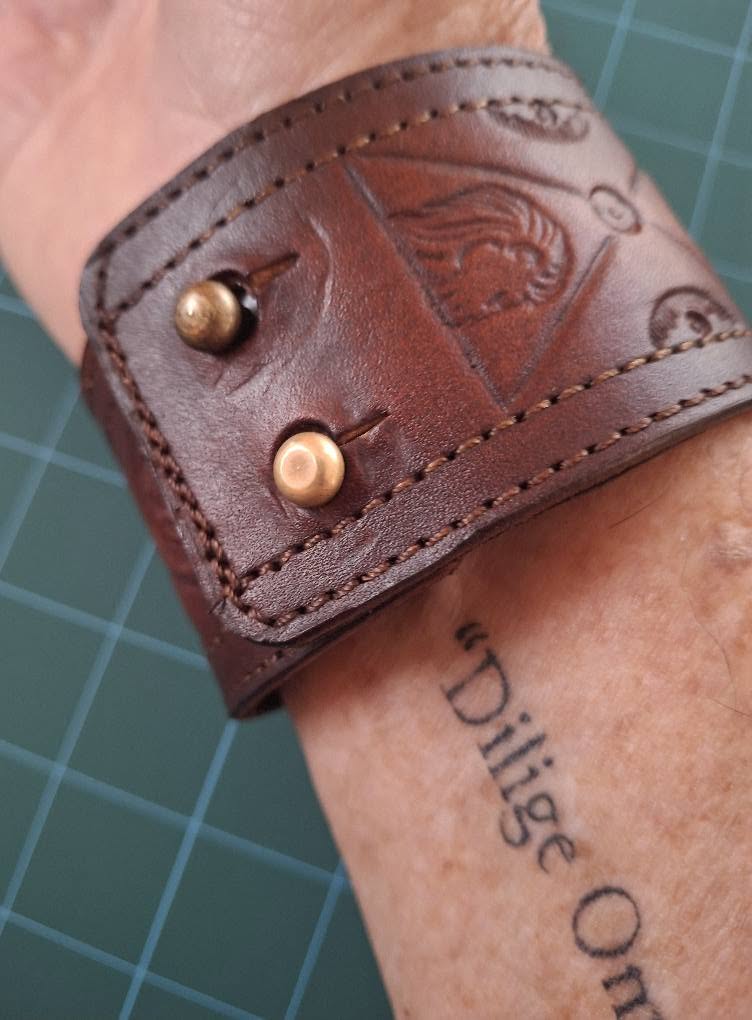 Stitched leather cuff with an embossed emblem, worn on the wrist