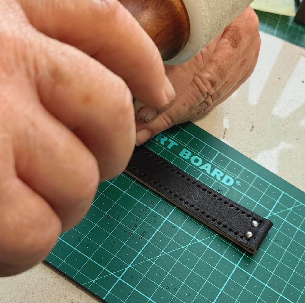 Jaco hand-stitching a black leather band at the workbench