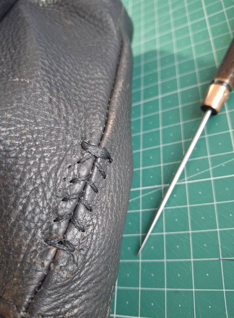Close-up of an awl and stitching on dark leather